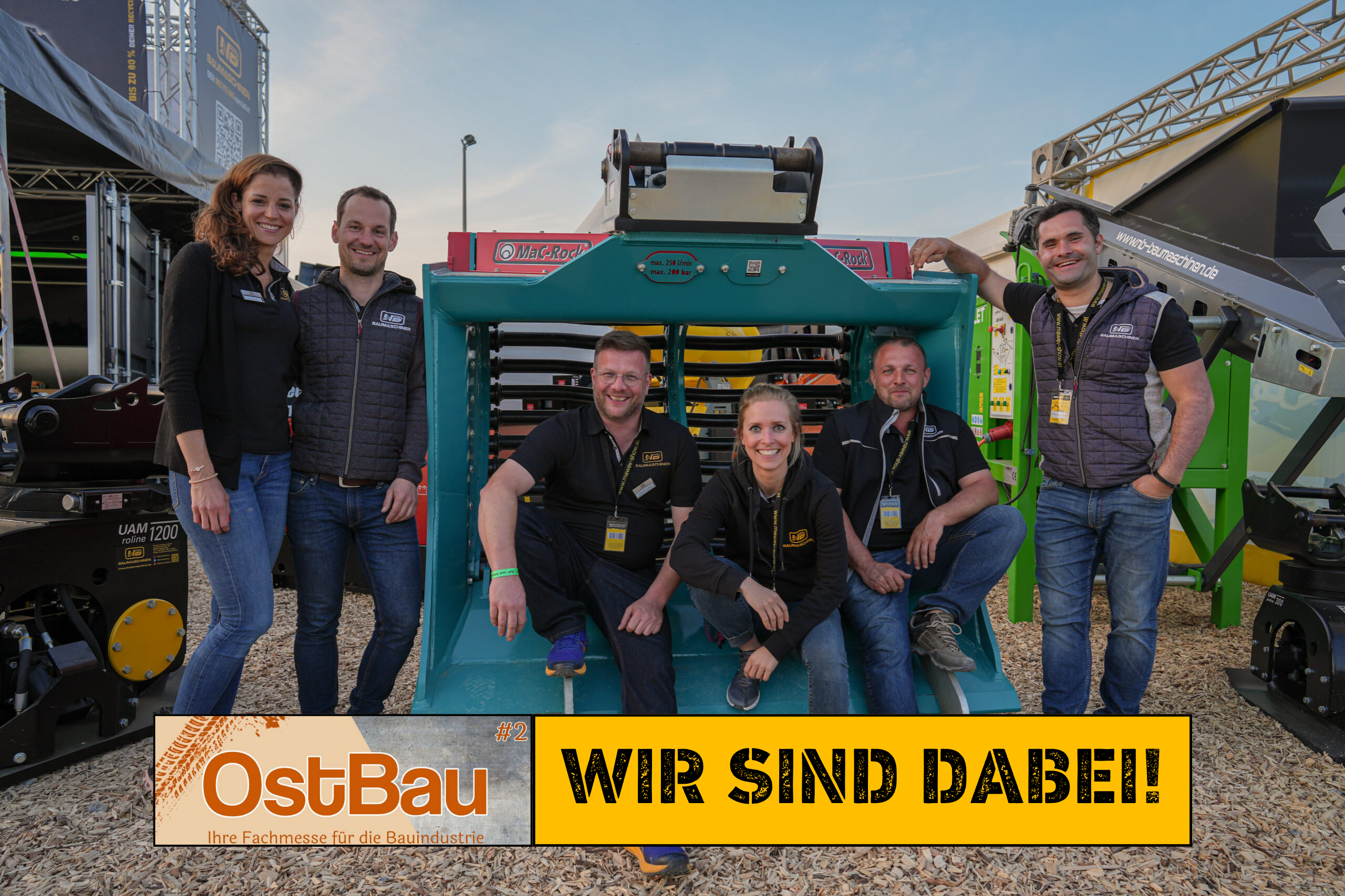 lachende menschen auf einem gruppenbild von einer baumesse, mit einem schaufelseparator und brechanlage. Die beschriftung lautet "Ostbau. Wir sind dabei!"