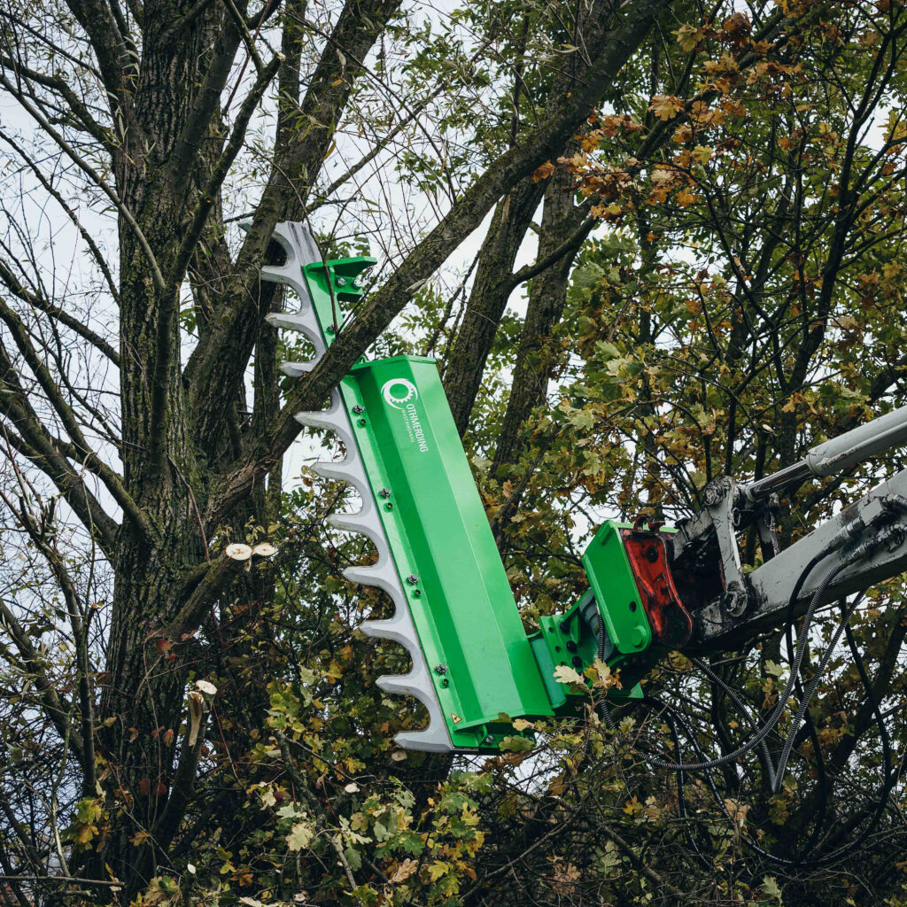 Eine grüne Ast- und Heckenschere von Othmerding greift in dichte Baumkronen, während hydraulische Arme und Metallzinken zwischen den Ästen ansetzen.