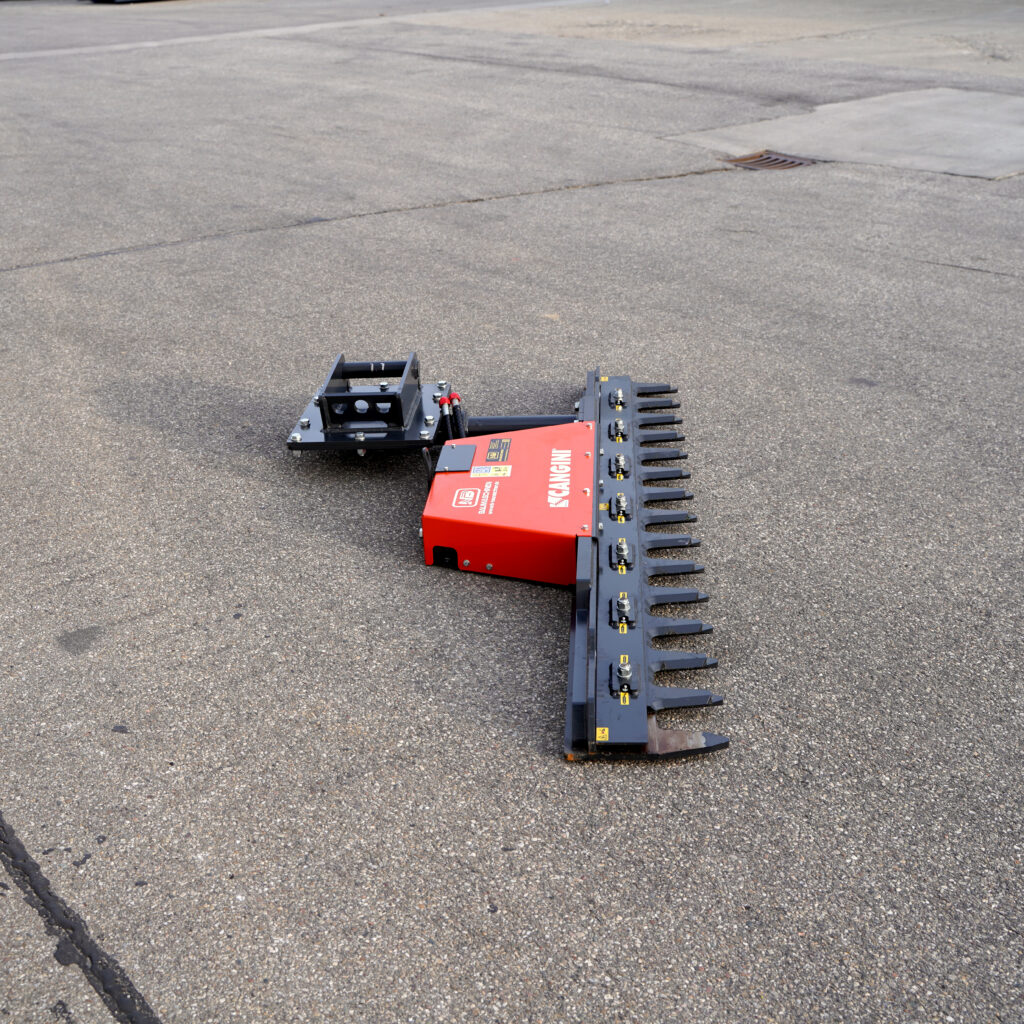 Ein rot-schwarzer Astscheren-Aufsatz liegt auf rauem Asphalt, mit langen Greifzinken und robustem Kupplungsrahmen für Baggerarbeiten.