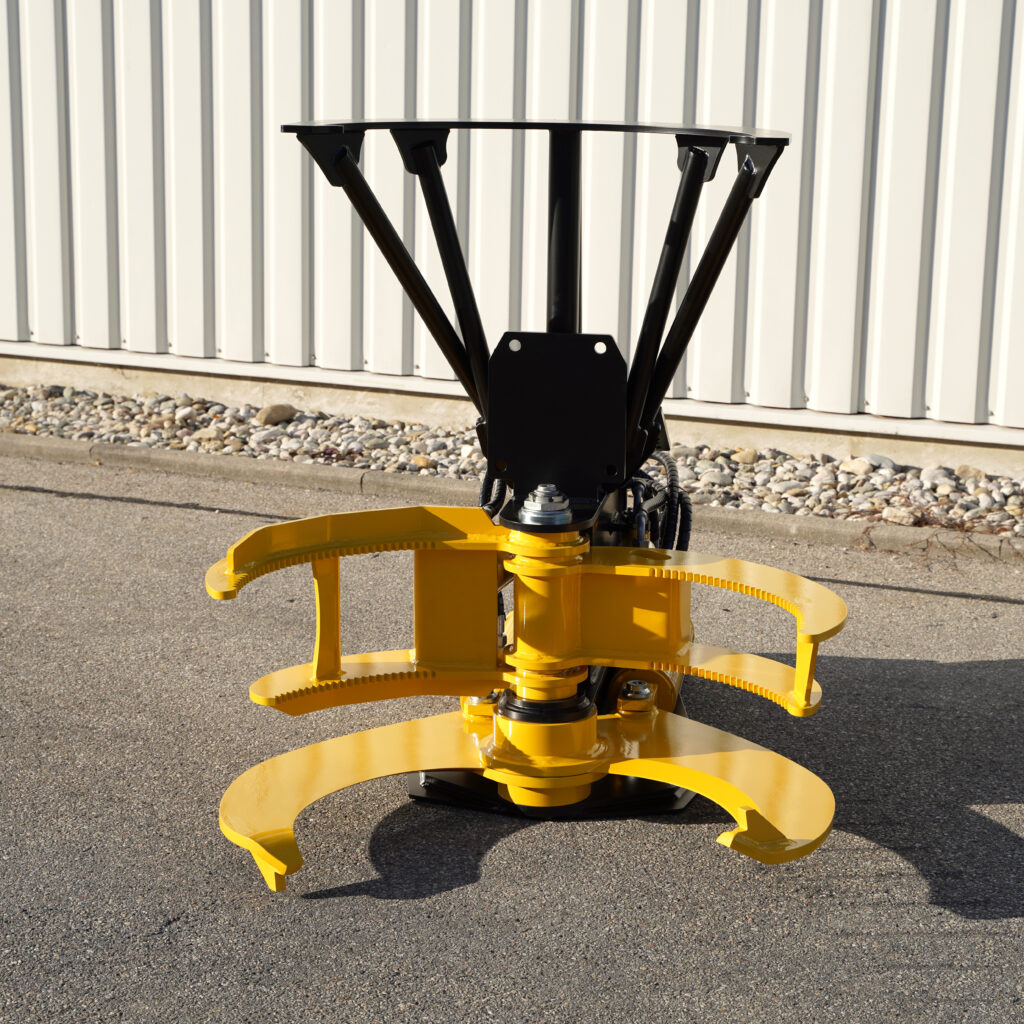 Schwarze Hydraulikarme und gelbe Greifbacken einer Baumschere stehen auf Asphalt vor einer hellen Metallwand mit Kiesstreifen im Sonnenlicht.