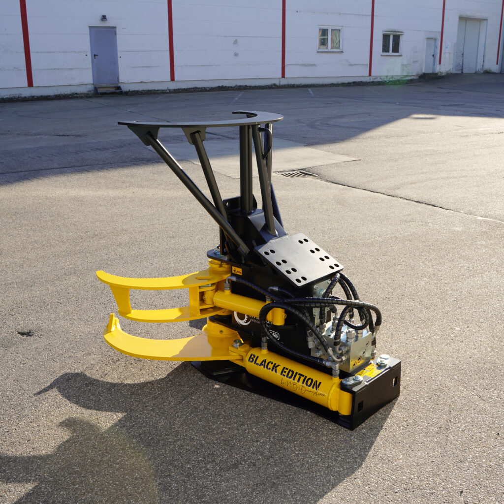 Gelb-schwarze Baumschere mit Hydraulikschläuchen, drei Greifarmen und schwerem Stahlrahmen steht auf Asphalt vor einer hellen Hallenwand.