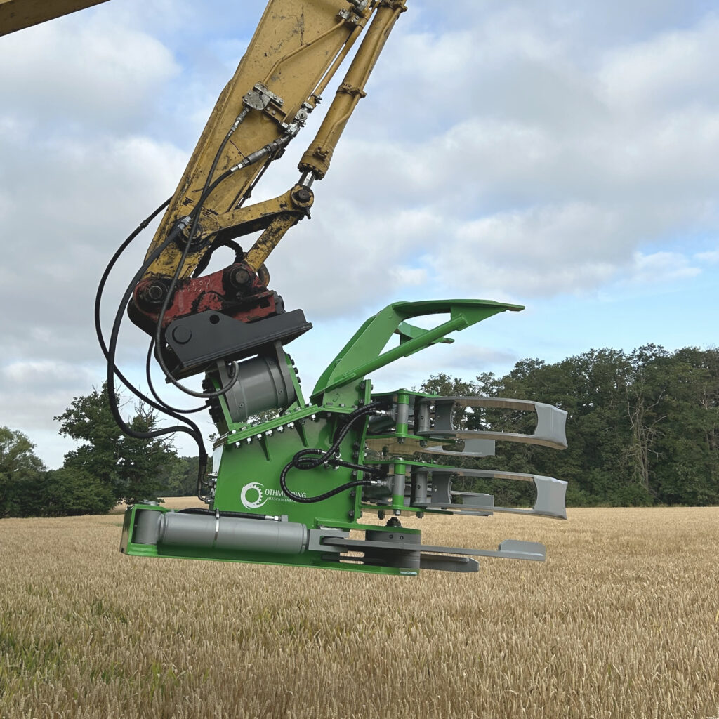 Grüne Baumschere BS-950-5 an einem Baggerarm mit gelbem Ausleger und Hydraulikschläuchen über einem Getreidefeld unter wolkigem Himmel.