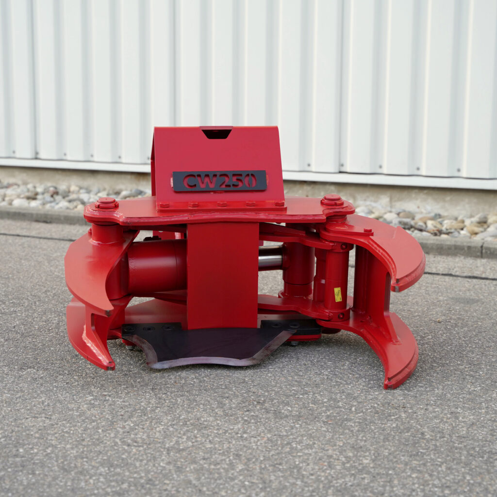 Rote Baumschere CW250 mit breiten Greifarmen und sichtbarem Hydraulikzylinder steht vor einer hellen Wellblechwand auf Asphalt.