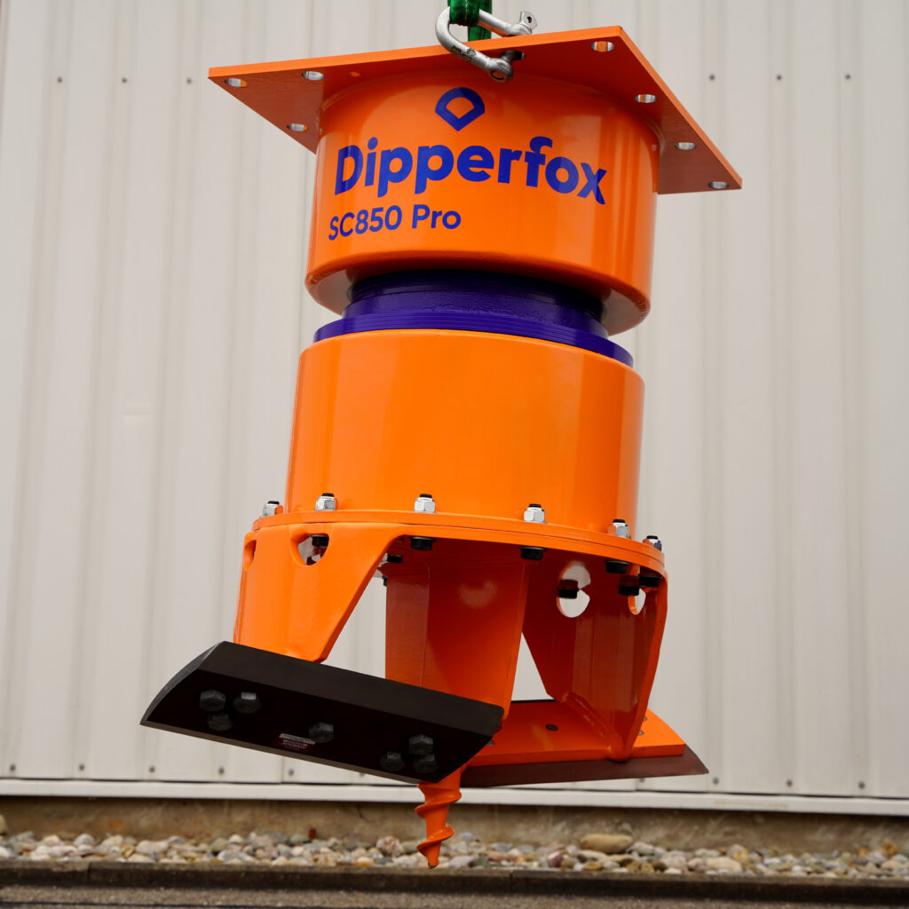 Der orangefarbene Dipperfox SC850 Pro hängt an einem Kranhaken vor einer hellen Metallwand, mit violettem Mittelteil und Bohrspitze unten.