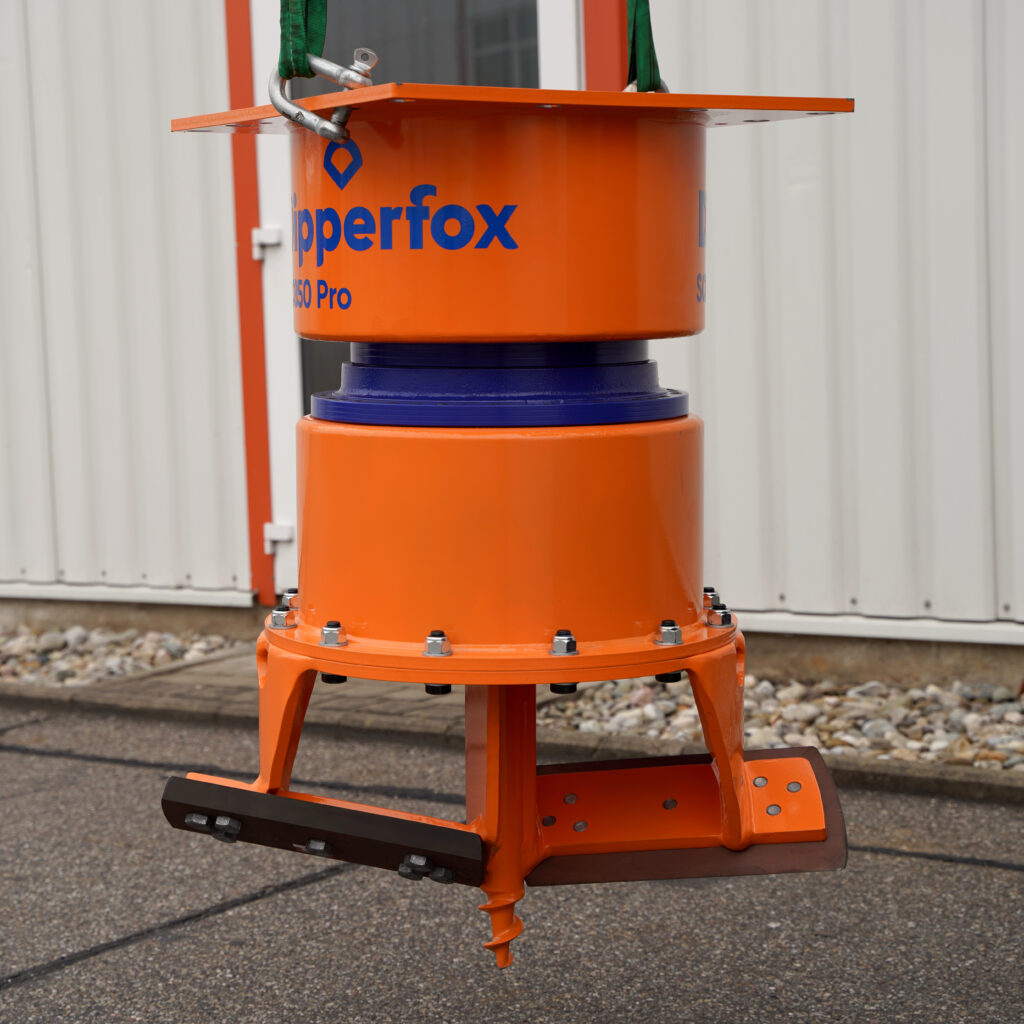 Orangefarbener Ripperfox SC850 Pro mit Bohrspitze und Schneidmessern hängt an Gurten vor einer Hallenwand und zeigt eine massive Stahlkonstruktion.