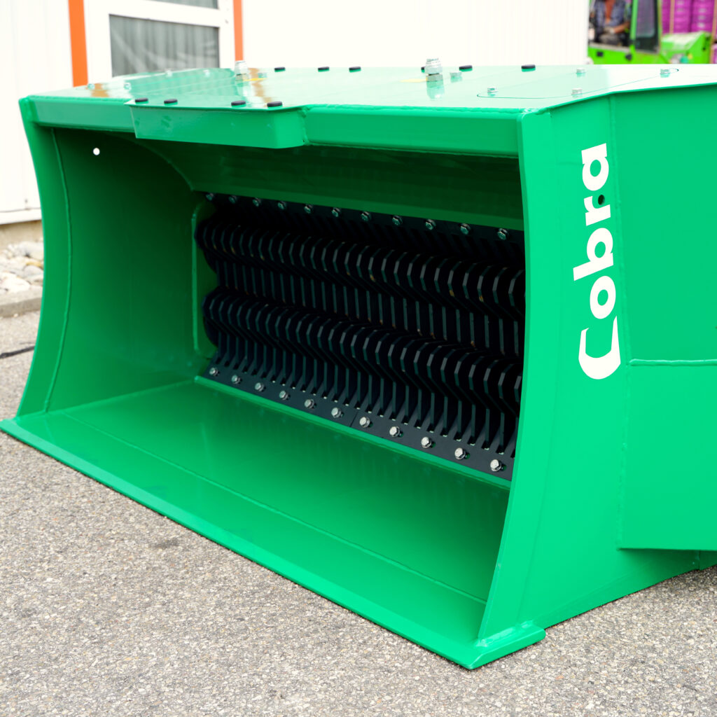 Der grüne COBRA-XS2-150-4 zeigt eine stabile Stahlkonstruktion mit schwarzem Schneidbereich und verschraubten Kanten vor hellem Untergrund.