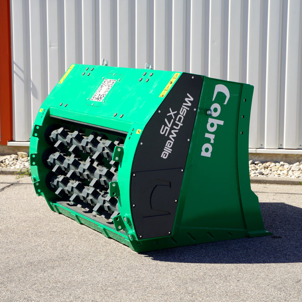 Ein grüner COBRA-Schredder mit schwarzen Seitenteilen und sichtbaren Rotorzähnen steht vor einer hellen Wellblechwand im Freien.