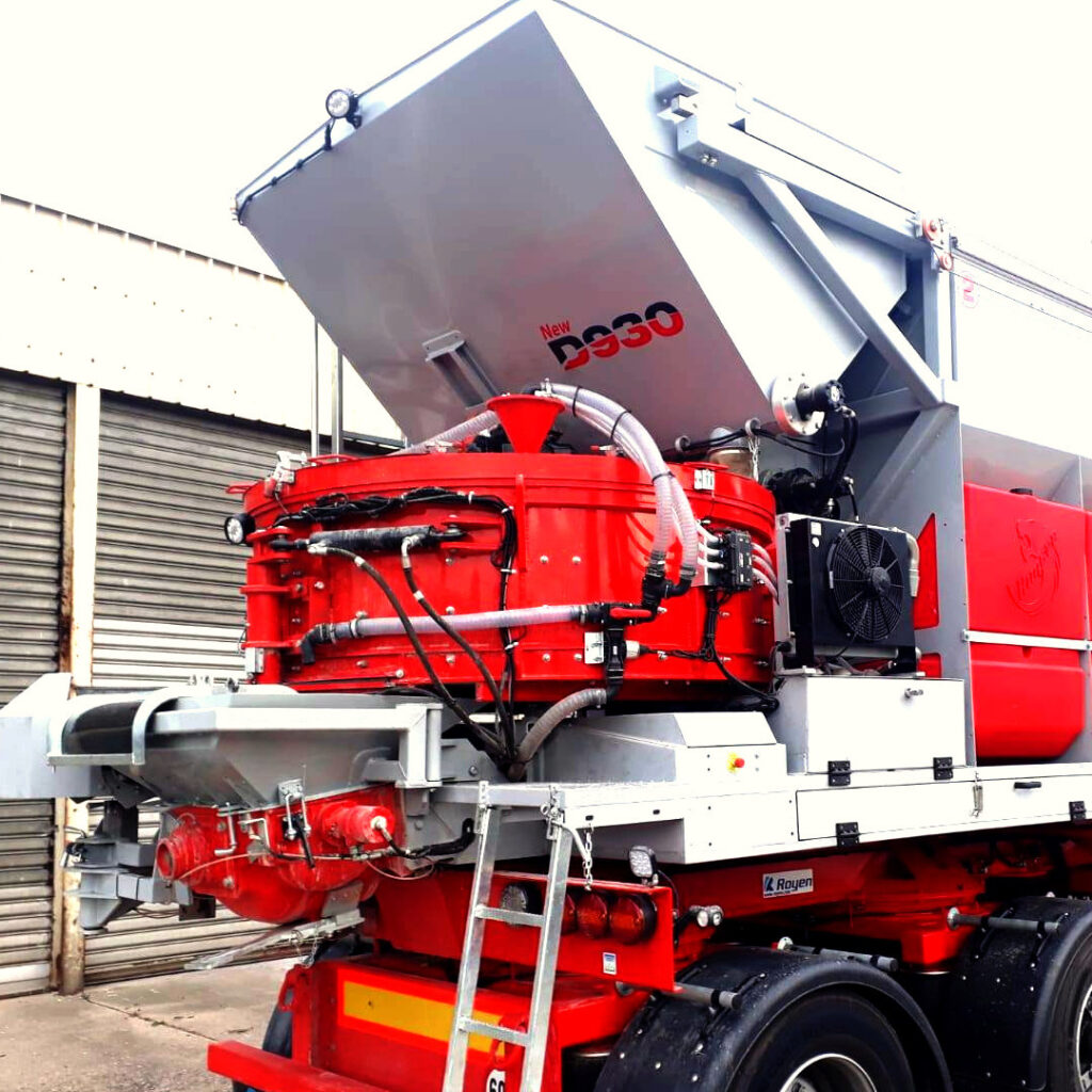 Eine rot-graue Recyclingmaschine mit großem Trichter, Schläuchen und seitlichem Lüfter steht vor einer Industriehalle; auf dem Trichter steht New D930.