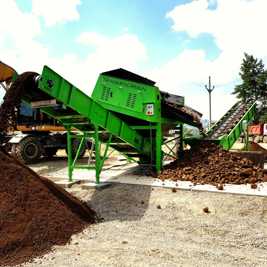 Ein grünes TRASERSCREEN-Siebgerät fördert auf einer Baustelle grobes Erdmaterial über mehrere Förderbänder, daneben liegen große Haufen aus Schotter und Boden.