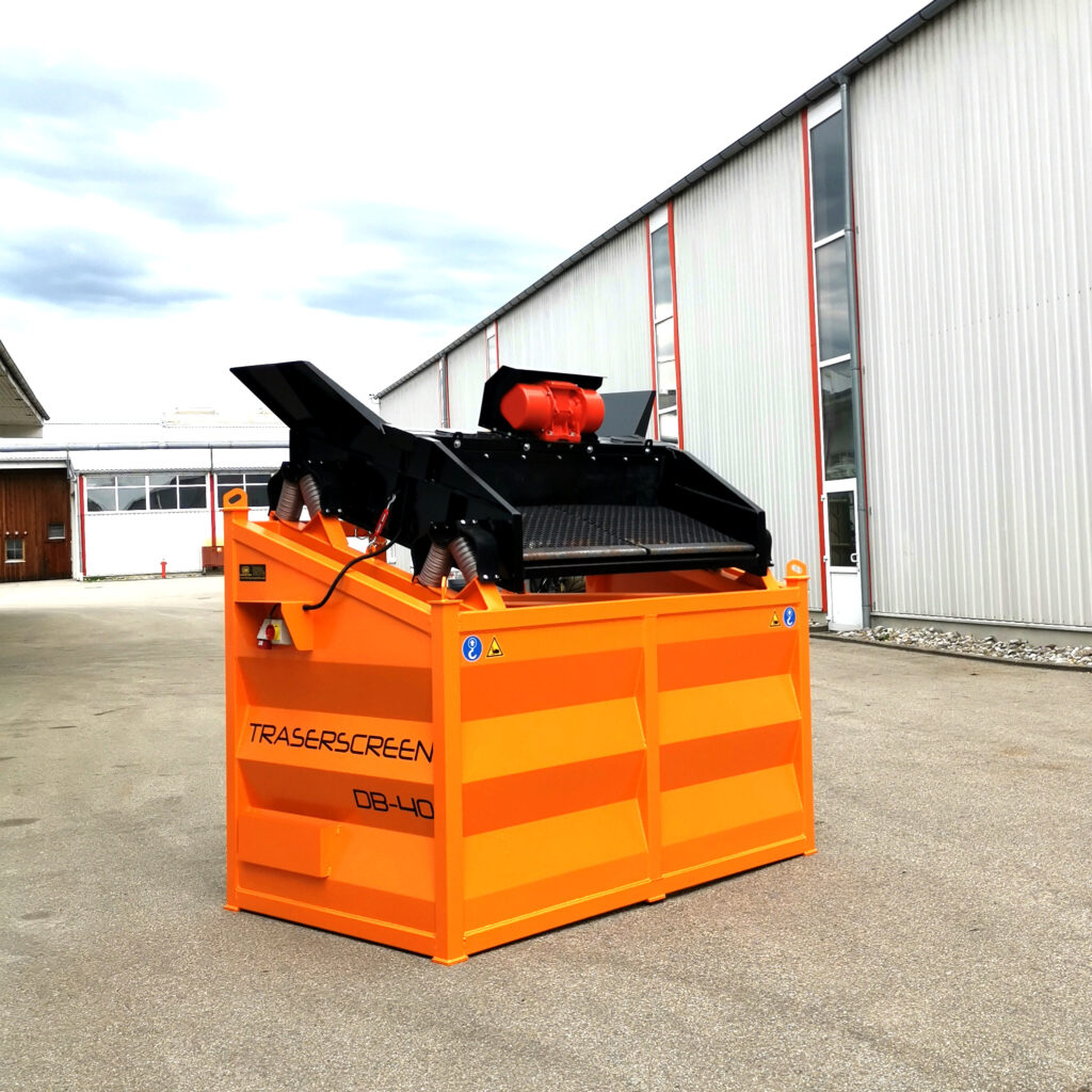 Vor einer Industriehalle steht ein orangefarbener TRASERSCREEN DB-40 mit schwarzer Siebeinheit und rotem Antrieb auf dem Hof bei hellem Himmel.