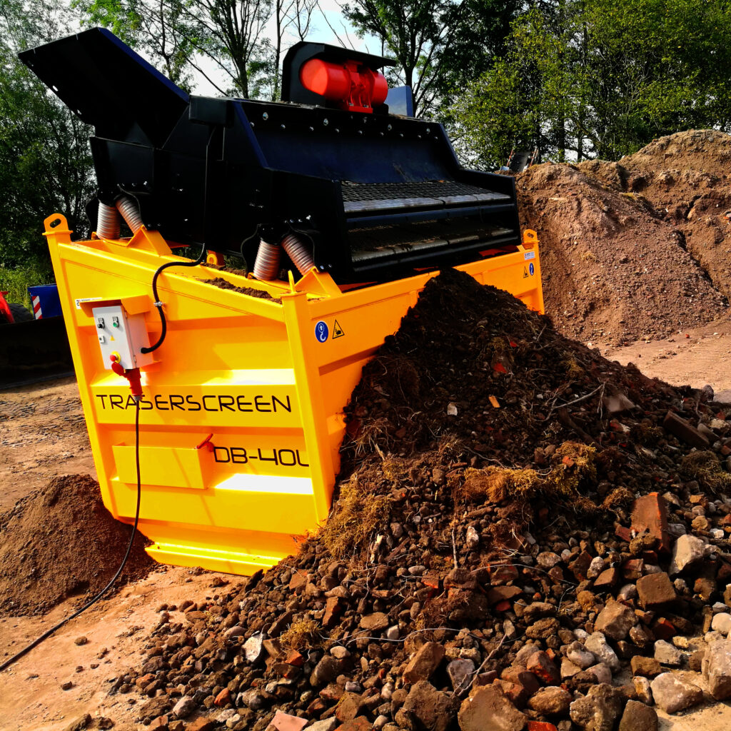Gelb-schwarzer DB-40L-6-Separator mit Trommel und Förderteilen arbeitet neben einem Haufen aus Erde, Steinen und Wurzelresten im Freien.