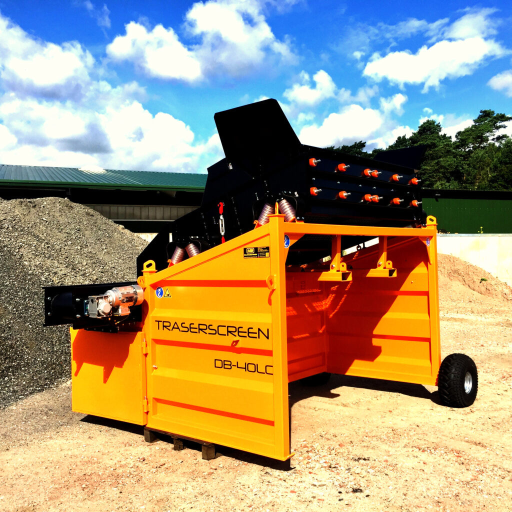 Das orange-schwarze TRASERSCREEN DB-40LC steht vor Schotterhaufen unter blauem Himmel, mit offener Klappe und sichtbaren Förderelementen.