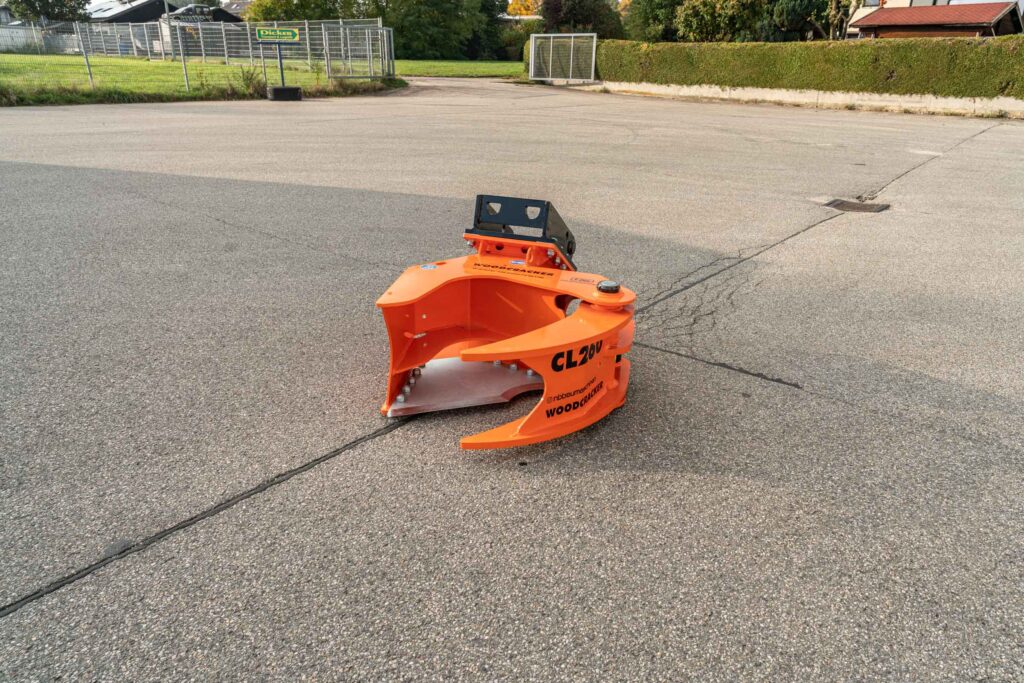 Ein orangefarbener WOODCRACKER CL 290 steht auf einem asphaltierten Hof, mit schwarzer Halterung und sichtbaren Kratzspuren am Metall.