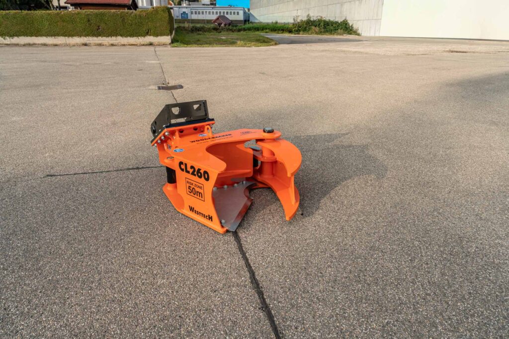 Orangefarbener Westtech Woodcracker CL260 mit schwarzer Halterung steht auf Asphalt vor einer Industriefläche mit Betonwänden und Grünstreifen.
