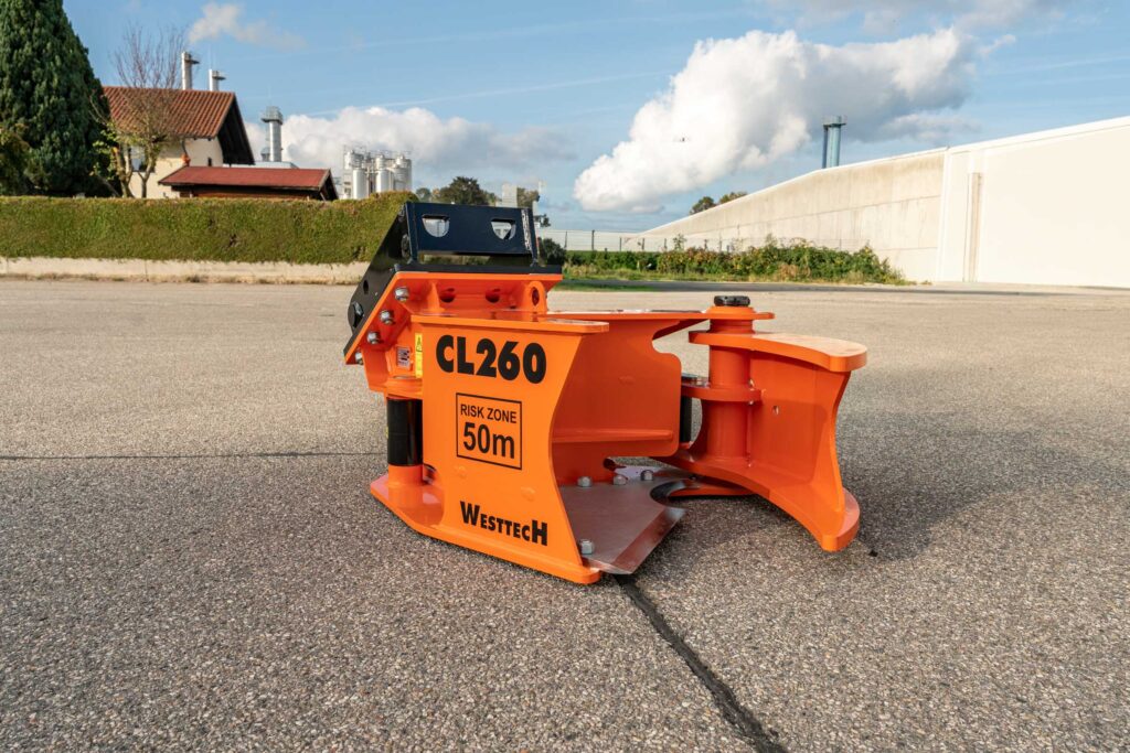 Orangefarbener Westtech CL260 mit schwarzem Aufnahmegestell steht auf Asphalt vor Industriegebäuden, unter blauem Himmel mit großen weißen Wolken.