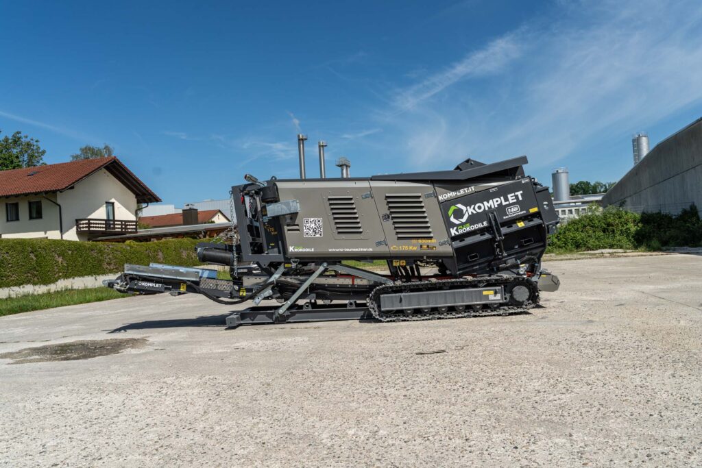Der mobile Schredder Komplet Krokodile PLUS steht auf Raupenfahrwerk vor blauem Himmel, mit grauer Verkleidung und sichtbaren Wartungsklappen.