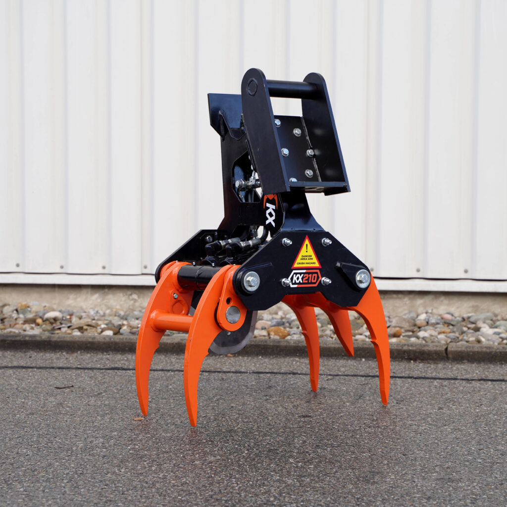 Der orange-schwarze Faellgreifer KX210 steht vor einer hellen Wand und zeigt vier lange Greifarme, massive Hydraulik und Warnaufkleber.