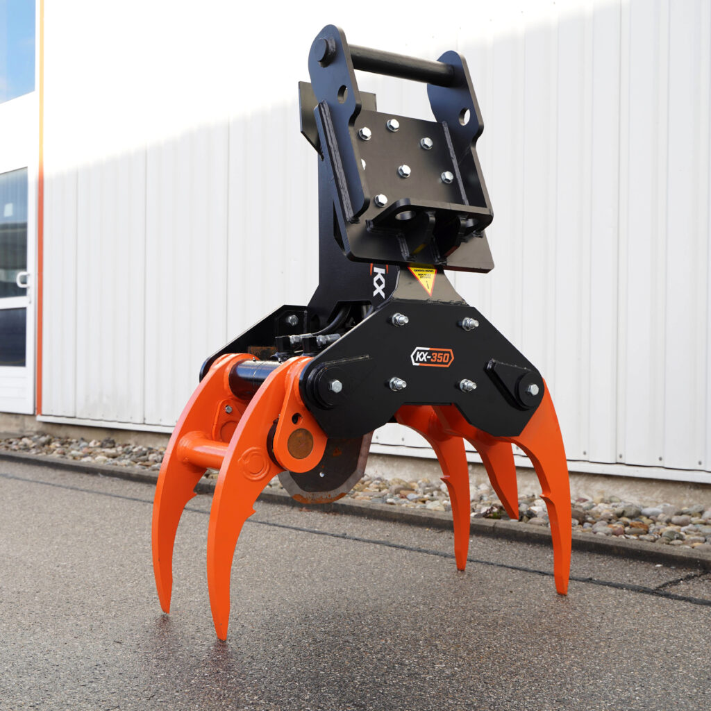 Ein schwarzer und orangefarbener Fällgreifer KX-350 mit massiven Greifarmen steht im Freien vor einer hellen Metallfassade auf nassem Asphalt.