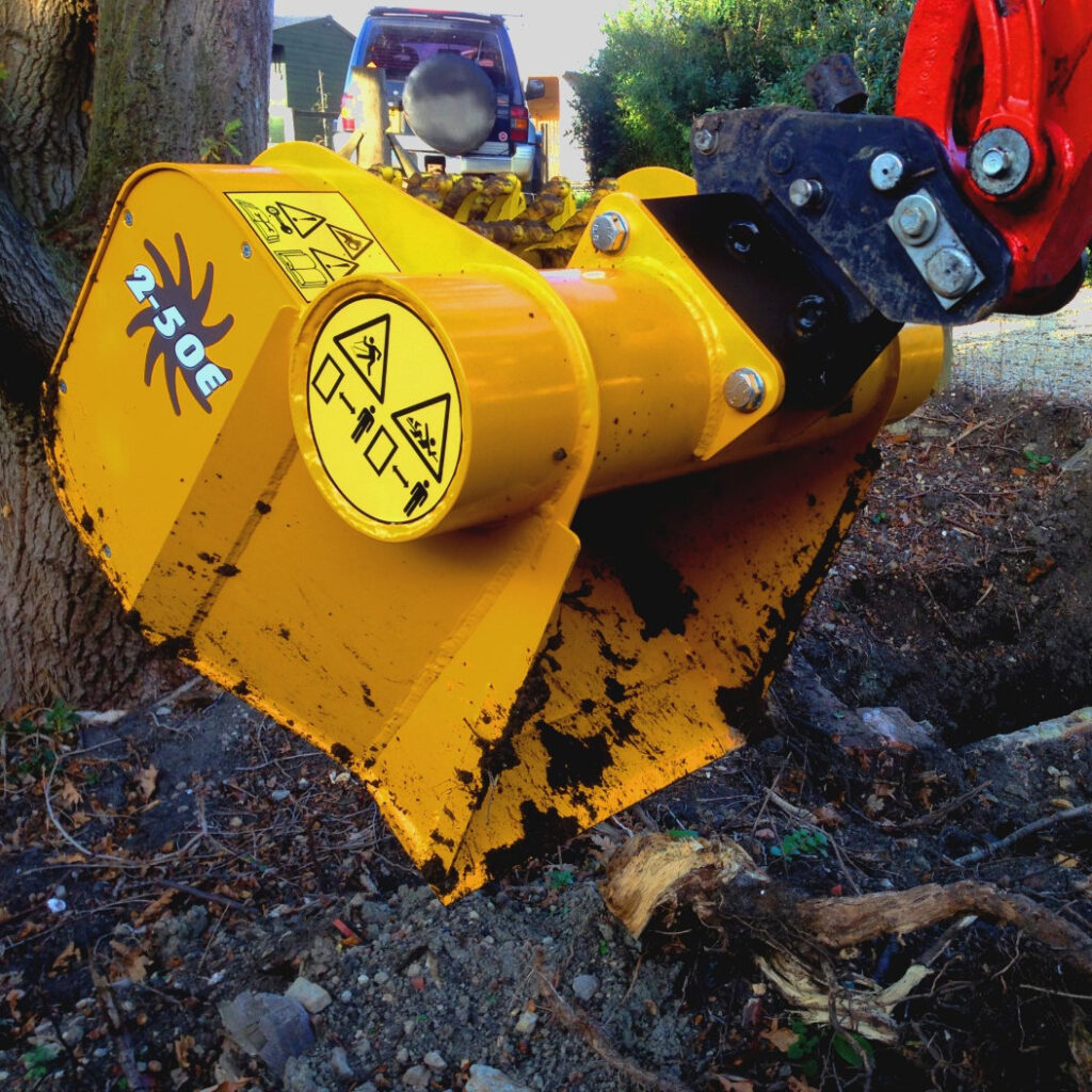 Ein gelber Gyru-Star 2-50E Recyclinglöffel greift an einem Baumstamm, während ein Baggerarm den Anbaugerätkopf im Einsatz hält.