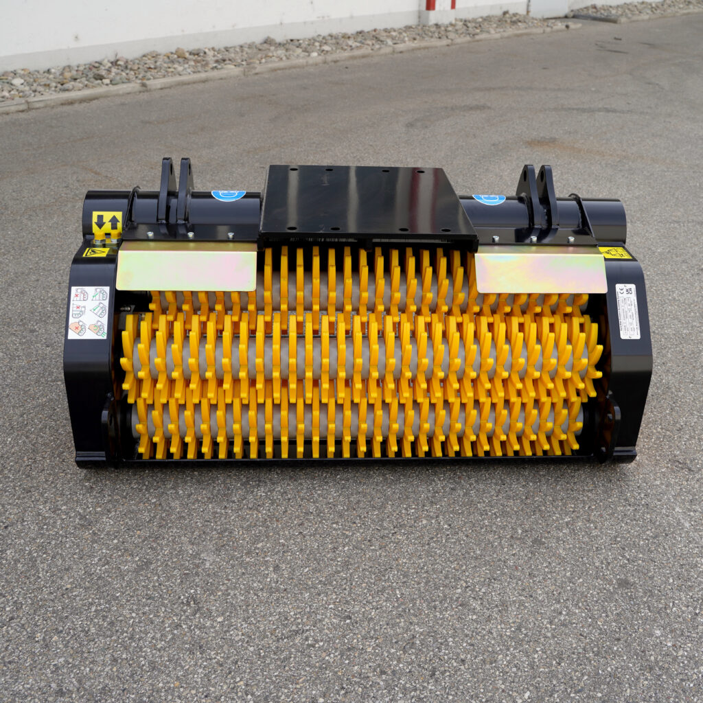 Ein schwarzer GYRUstar 3-120HE-5 mit gelben Zerkleinerungselementen steht auf Asphalt vor einer weißen Wand und zeigt robuste Stahlaufnahmen.