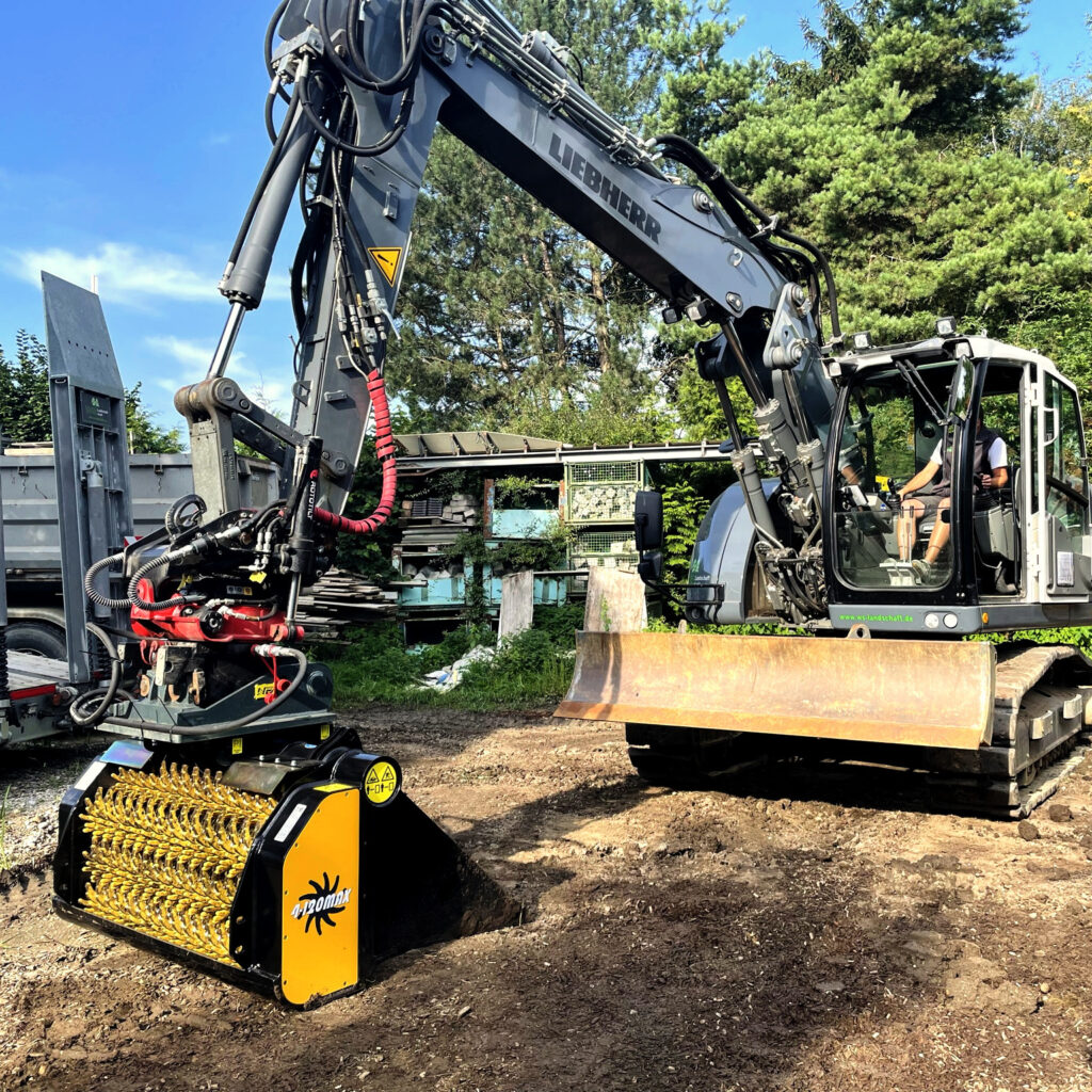 Ein Liebherr-Bagger steht im Freien neben einem gelb-schwarzen Arbomax-Anbaugerät, während der Ausleger über dem Arbeitsbereich schwebt.