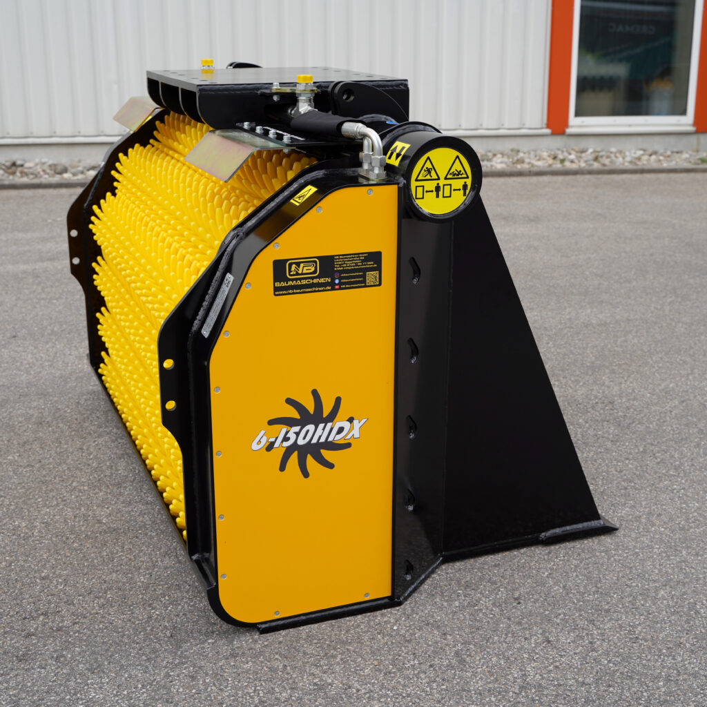 Der gelb-schwarze GYRUstar 6-150HDX von NB Baumaschinen steht mit breiter Schutzkante und gelben Borsten auf grauem Asphalt vor einer Halle.