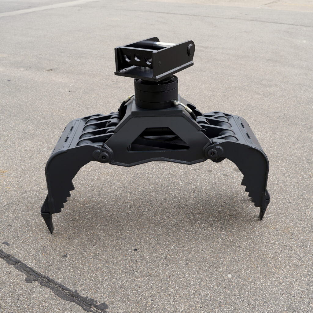 Ein schwarzer hydraulischer Greifer mit drei gebogenen Greifarmen steht auf Asphalt, darüber sitzt ein massiver Drehkranz mit Anschlüssen.