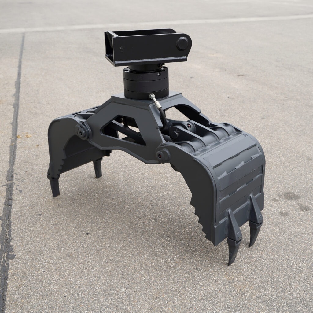 Ein schwarzer Hydraulikgreifer mit massiven Greifarmen, Drehkopf und Zähnen steht auf grauem Asphalt vor einem hellen, ruhigen Hintergrund.