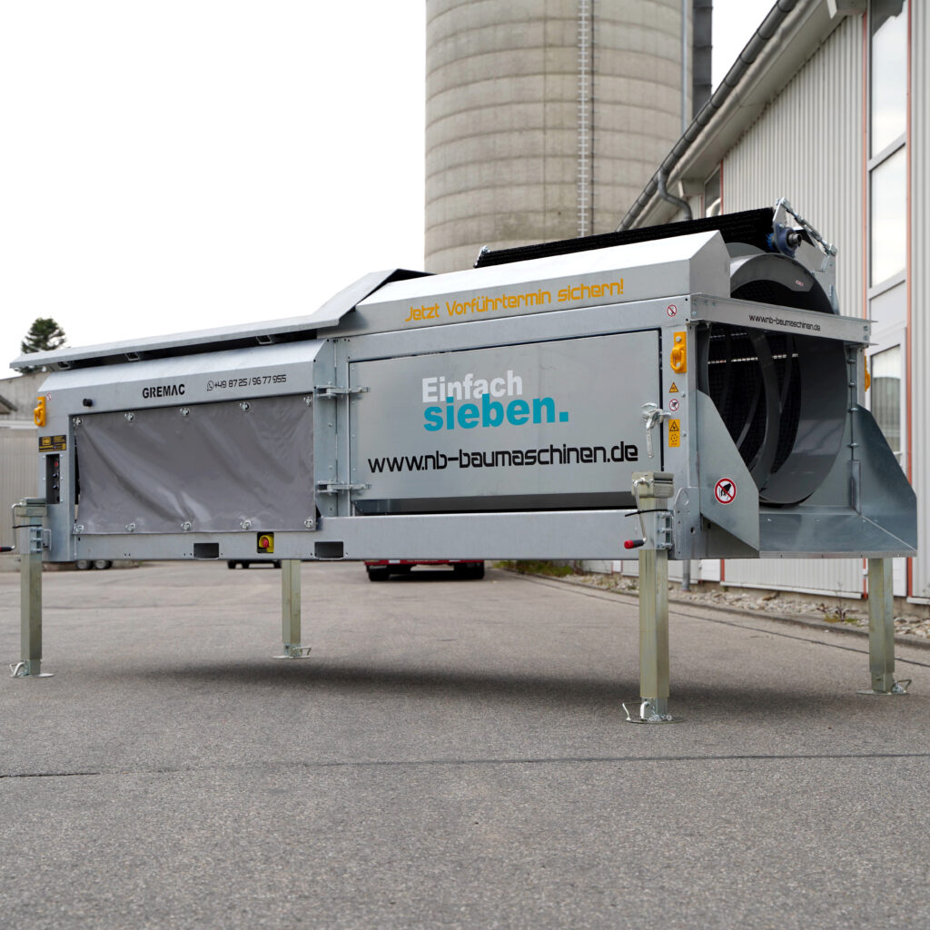Ein grauer Gremac eZero-Siebroboter steht vor einer Industriehalle, daneben ein Siloturm; auf dem Gehäuse sind Marken- und Webaufdrucke zu sehen.