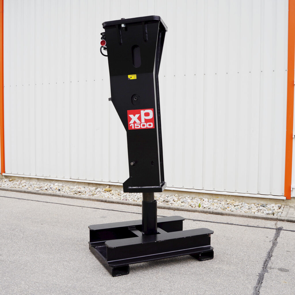 Ein schwarzer Hydraulikhammer mit rotem XP-1500-Logo steht vor einer weißen Industriewand auf Asphalt und zeigt seine massive, kantige Bauform.