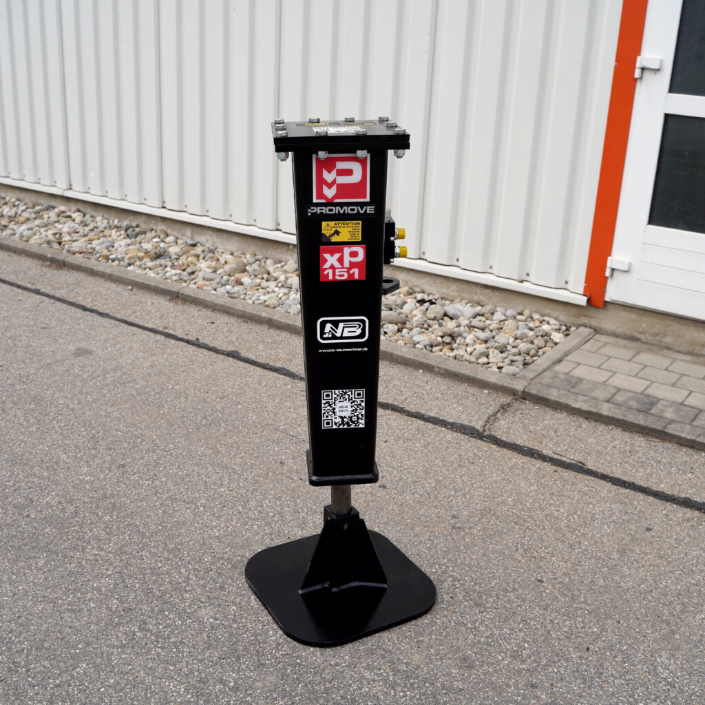 Vor einer hellen Metallfassade steht ein schwarzer Promove XP151-2 Hydraulikhammer auf einer breiten Stahlplatte, mit Warnaufkleber und QR-Code.