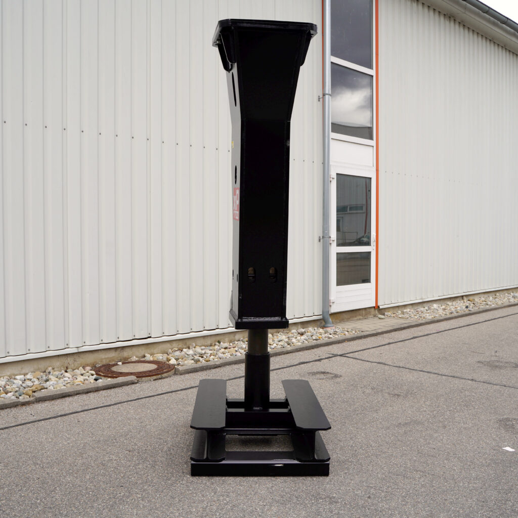 Ein schwarzer Hydraulikhammer XP1700-4 steht aufrecht vor einer hellen Industriehalle und zeigt seinen massiven Stahlkörper mit breitem Fuß.