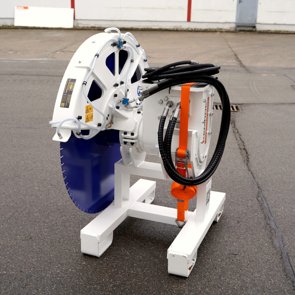 Die weiße Kemroc Steinsäge KDS30-1 steht auf einem Metallgestell, mit blauem Sägeblatt, schwarzen Hydraulikschläuchen und orangefarbenem Spanngurt.