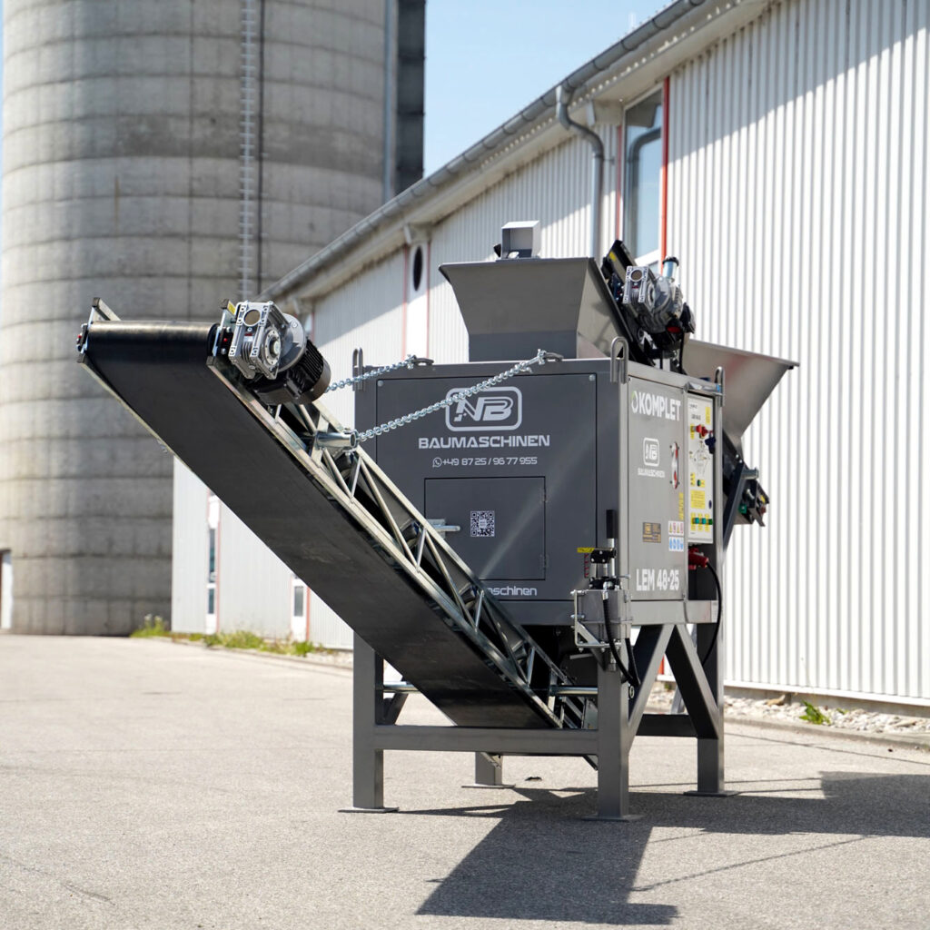 Graue Recyclingmaschine LEM 48-25 mit zwei Förderbändern steht vor einer hellen Industriehalle, daneben ein großes Silos und klarer Himmel.