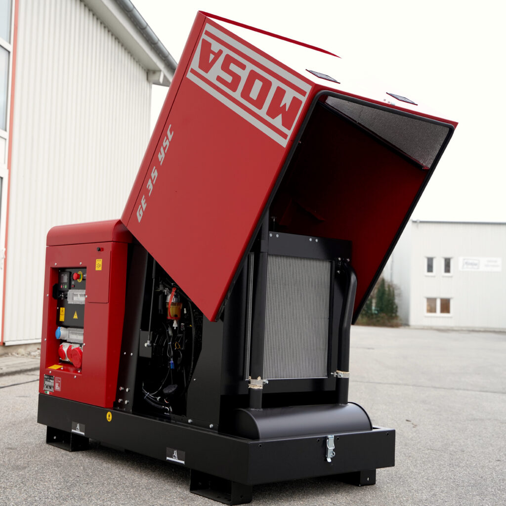 Ein roter MOSA GE35YSC-5 Stromerzeuger mit geöffneter Haube steht vor einem Industriegebäude, wobei Technik und Kühlmodule sichtbar sind.