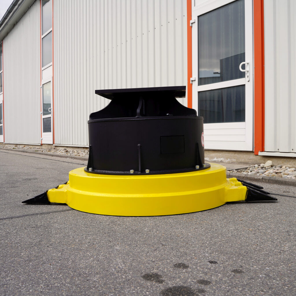 Schwarze und gelbe Stahlkomponente mit breiter Rundform steht vor einer hellen Industriehalle mit orangefarbenen Akzenten und Fenstern.