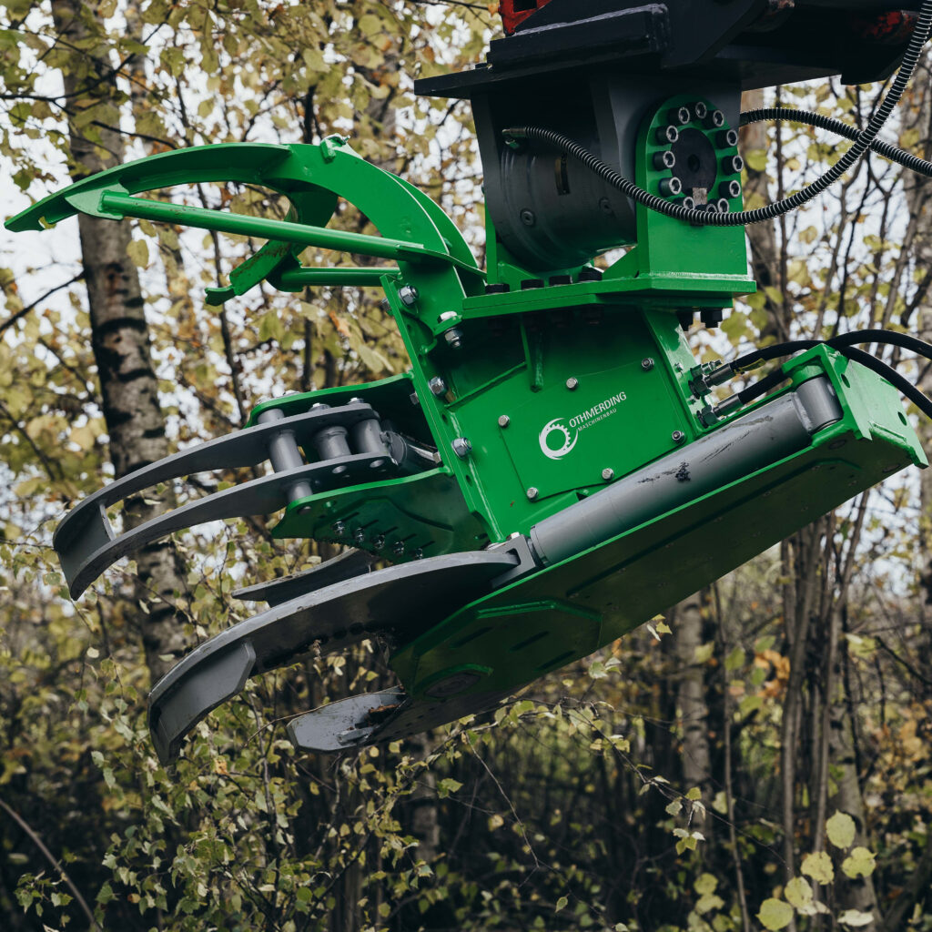 Die grüne Othmerding-Baumschere mit Greifarmen und Hydraulikschläuchen hängt vor herbstlichen Bäumen und zeigt robuste Stahltechnik im Einsatz.