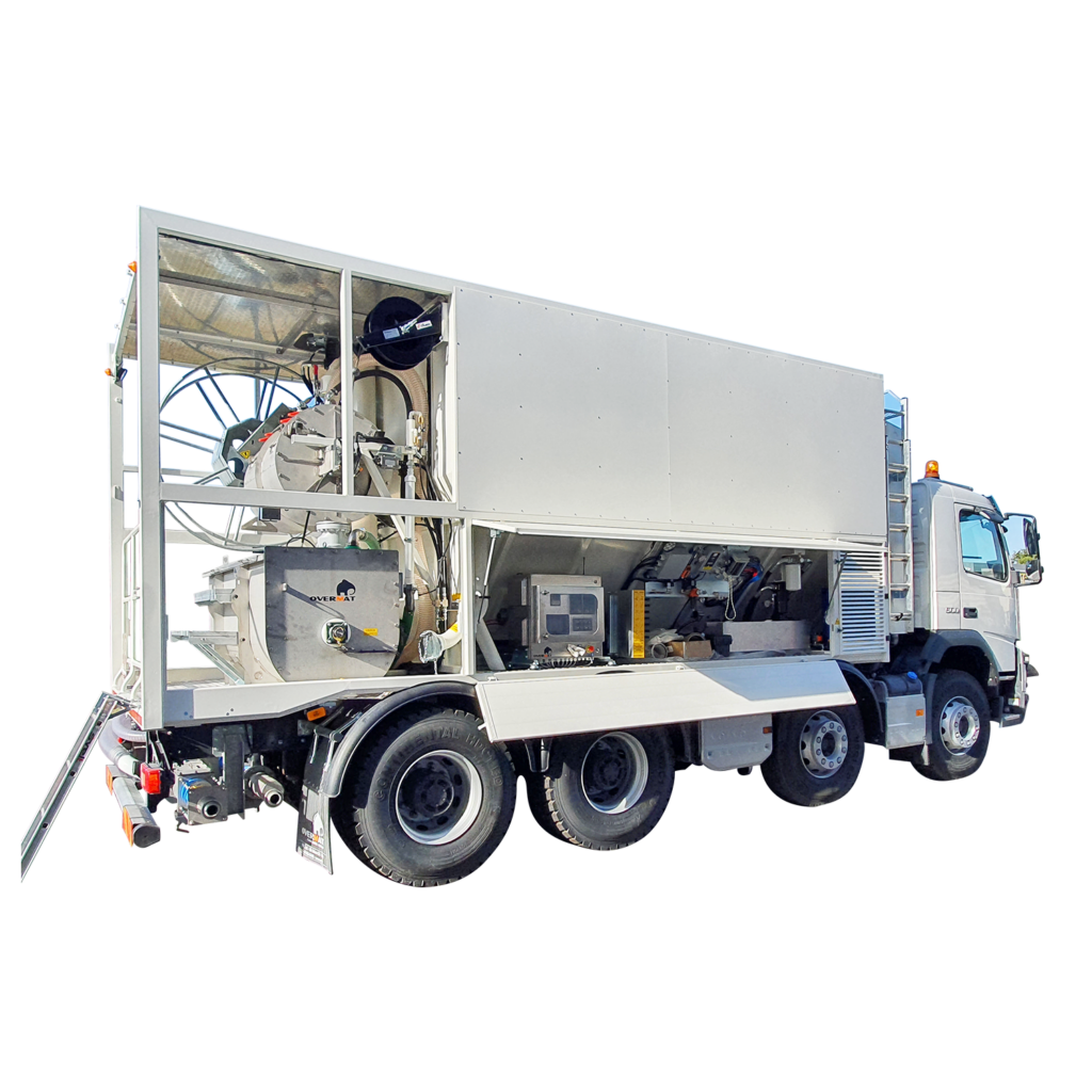 Ein weißer Overmat-Mischtruck mit offenem Aufbau zeigt Tanks, Leitungen und Steuertechnik neben der Kabine vor klarem Himmel im Freien.