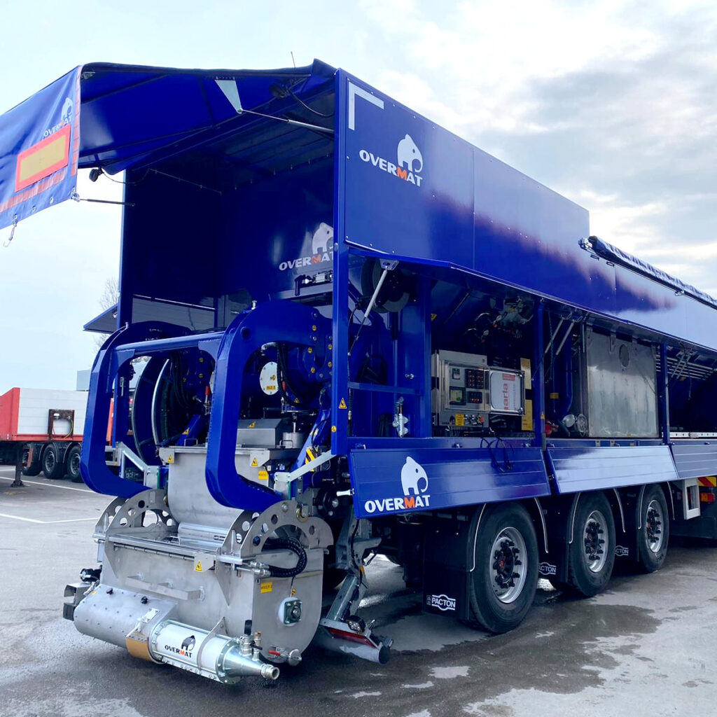 Ein blauer Overmat Series ALS Fließestrich-Mischer steht auf einem Lkw-Auflieger mit sichtbaren Hydraulik-, Pumpen- und Steuerkomponenten unter wolkigem Himmel.