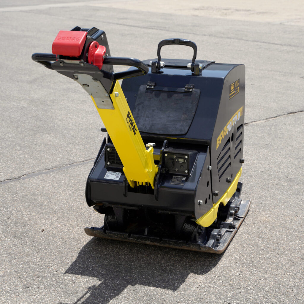 Die gelb-schwarze Bomag BPR 70-70D steht auf Asphalt und zeigt den roten Motorhaubenbereich, den Tragegriff und die massive Stahlplatte.