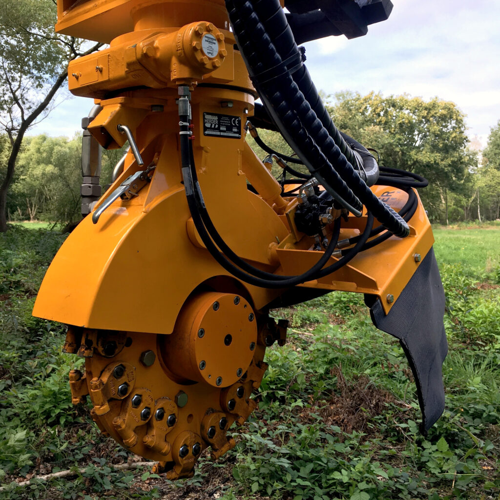 Ein orangefarbener SCE-550H mit dicken Hydraulikschläuchen und robustem Schneidkopf steht auf einer lichtdurchfluteten Waldlichtung.