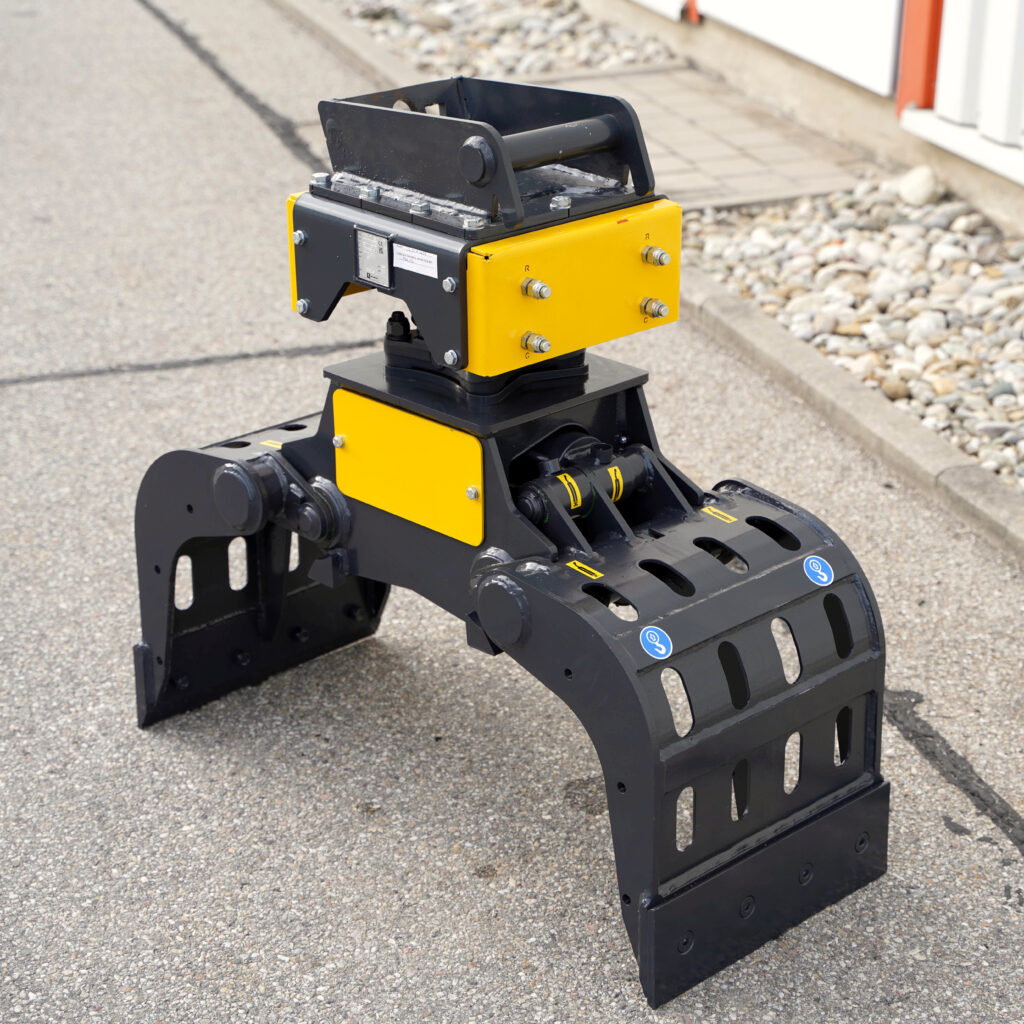 Ein schwarz-gelber Sortiergreifer PF150-5 steht auf Asphalt vor einer hellen Gebäudefassade mit Steinen am Rand und sichtbaren Hydraulikanschlüssen.