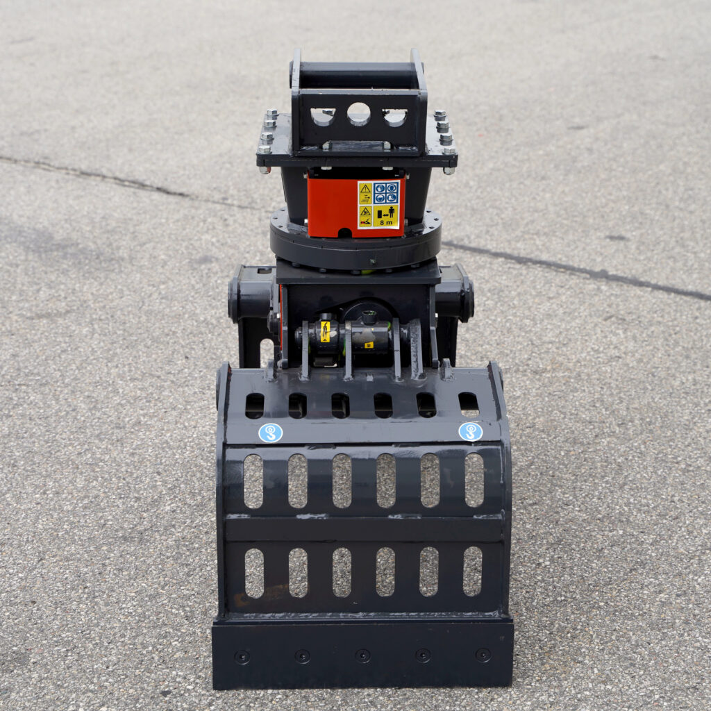 Ein schwarzer Sortiergreifer PF200-5 mit rotem Mittelgehäuse und Warnaufklebern steht auf rauem Asphalt vor hellem, unscharfem Hintergrund.