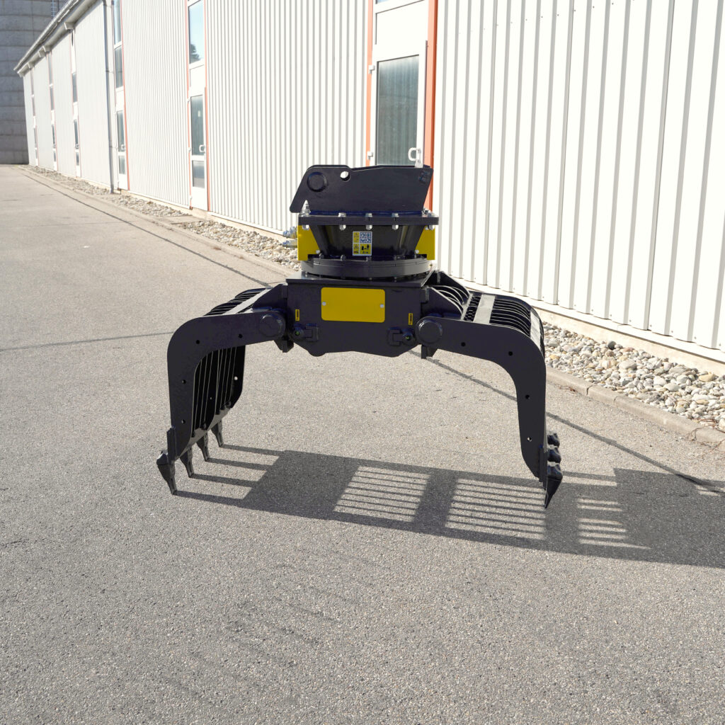Ein schwarz-gelber Sortiergreifer PG450-4 steht auf Asphalt vor einer hellen Hallenfassade mit langen Metallwänden und scharfen Schatten.