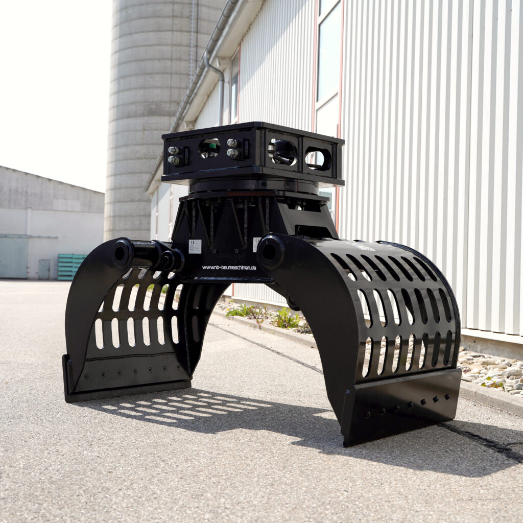 Großer schwarzer Sortiergreifer mit breiten Greifarmen steht vor einer Industriehalle, daneben Betonsilo und helle Fassaden mit vertikaler Verkleidung.