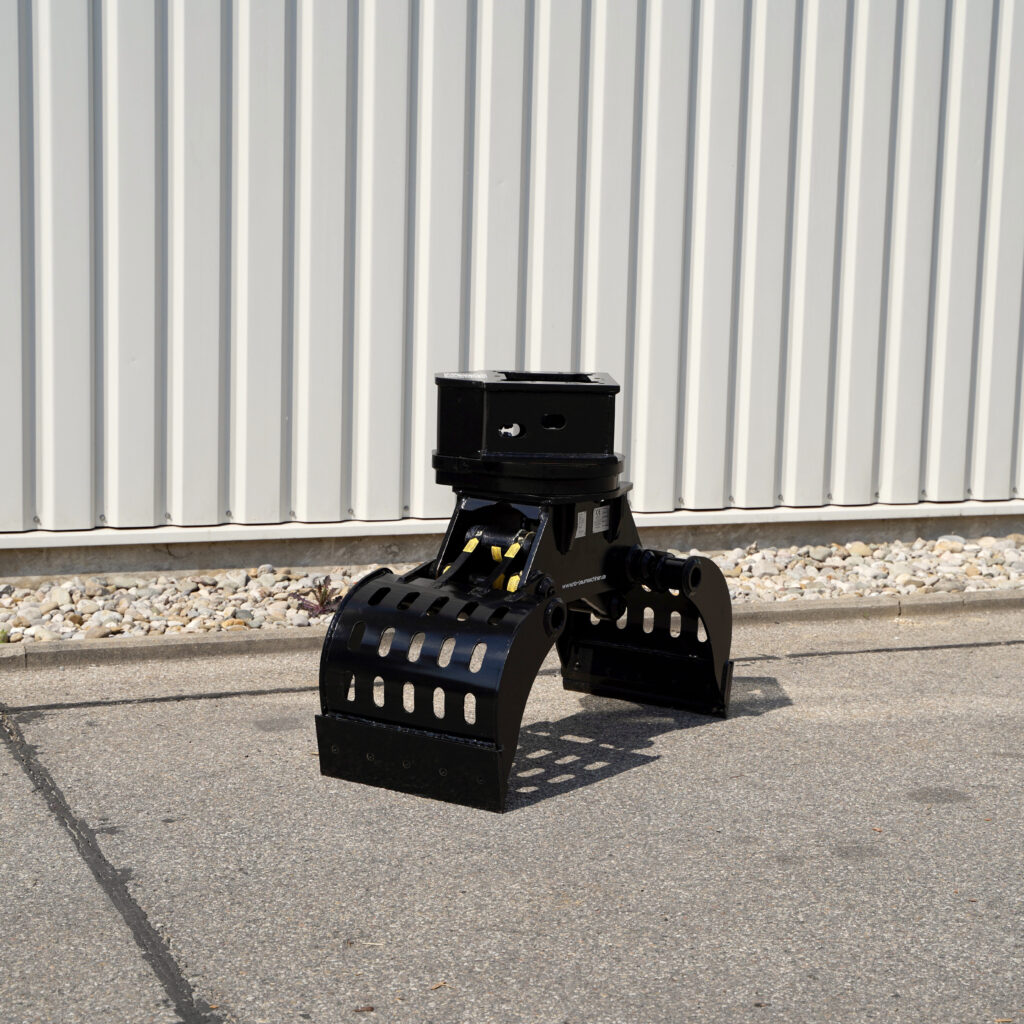 Der schwarze Sortiergreifer SG3.4-3 steht auf Asphalt vor einer hellen Metallfassade und zeigt seine breiten Greifarme mit vielen Schlitzen.