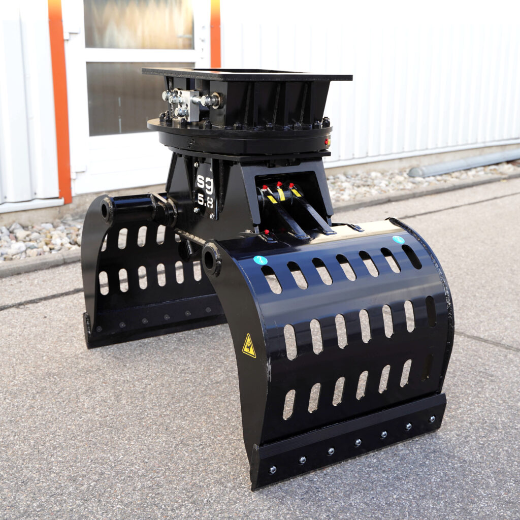Der schwarze Sortiergreifer SG5.8-2 steht auf dem Asphalt vor einer Halle und zeigt breite Greifarme, Schlitzöffnungen und robuste Hydraulik.