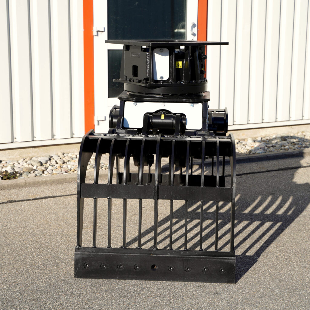 Der schwarze Sortiergreifer SM-100-1 steht vor einer hellen Metallfassade und zeigt vorne breite Greifzinken sowie eine massive Drehaufnahme.