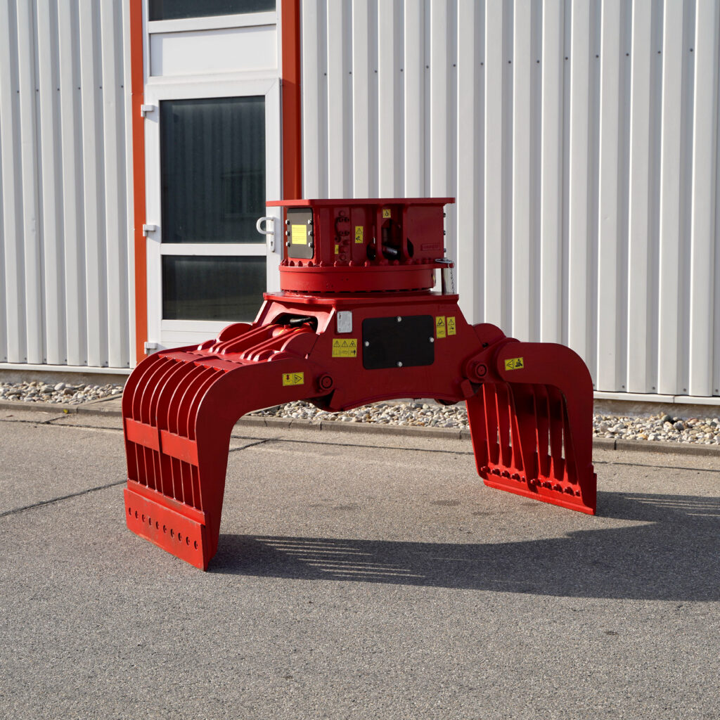 Ein roter Sortiergreifer SM-120-2 steht vor einer hellen Metallfassade auf Asphalt, mit breiten Greifarmen, Warnaufklebern und klaren Kanten.