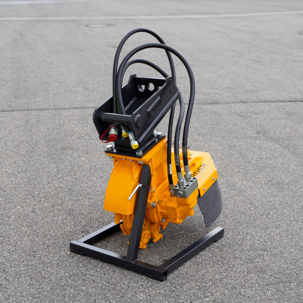 Ein gelb-schwarzer Stubbenfräsen-Aufsatz SCE-410H-5 steht auf Asphalt, mit mehreren Hydraulikschläuchen, Metallrahmen und Anschlussblock.